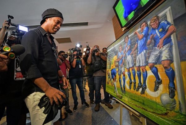Brazilian former footballer, Ronaldinho (L) looks at a painting by artist Emerson Carvalho de Souza, during a photocall to unveil memorabilia and artworks including his Barcelona football jersey at Maracana stadium in Rio de Janeiro, Brazil, on February 28, 2019. PHOTO/AFP