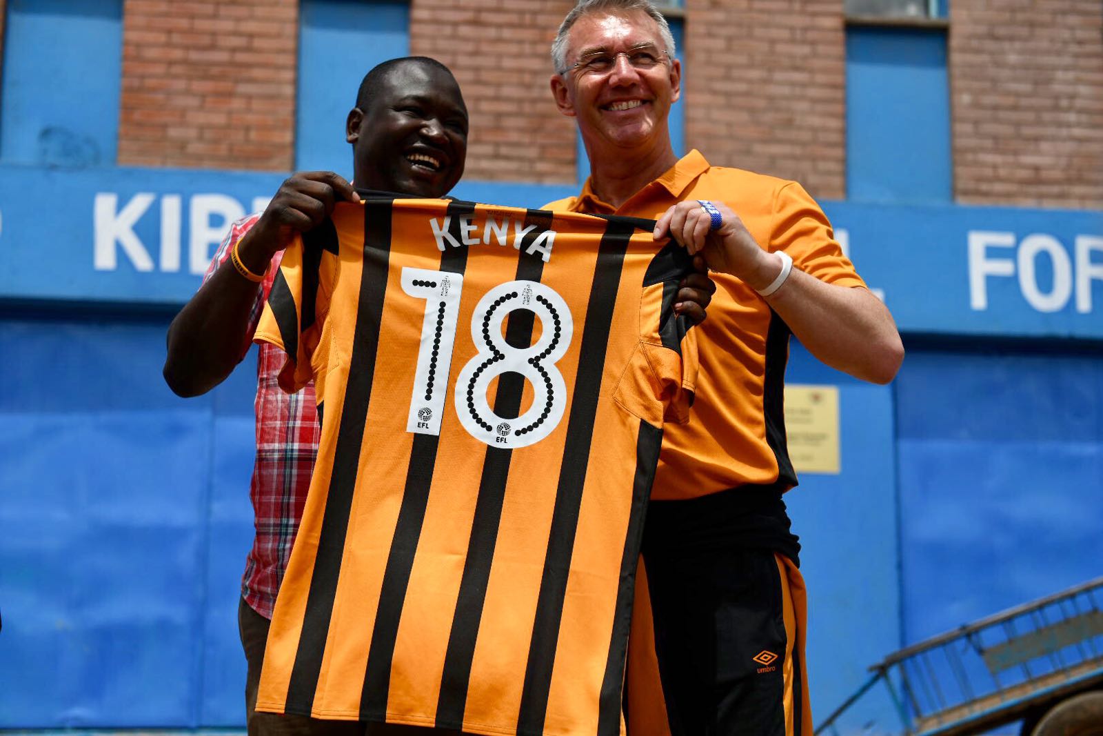 Hull City FC manager, Nigel Adkins present a branded shirt to Shofco FC founder, Kennedy Odede, when the team visited sprawling Kibera slum in Nairobi, Kenya, in May, 2018.PHOTO/SPN