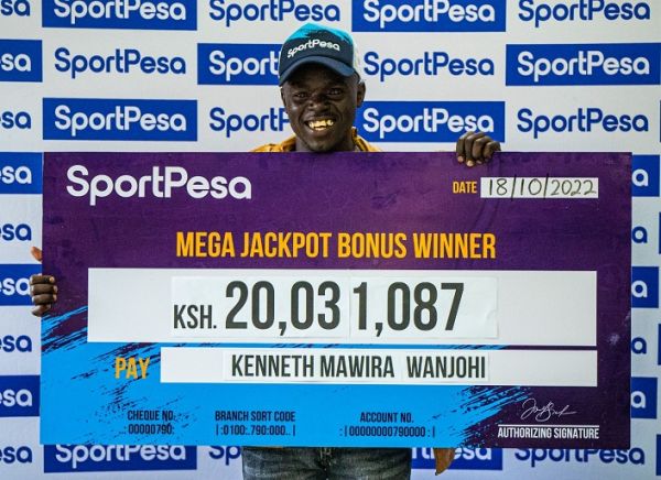 Kenneth Wanjohi poses with his winners cheque after winning a bonus of over KSHs 20 million in the SportPesa Mega Jackpot on Tuesday, October 18, 2022. PHOTO | SPN