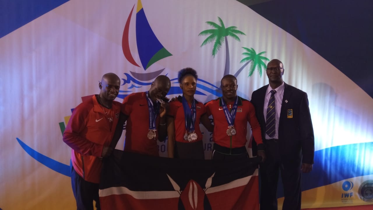 L to R: Kenya weightlifting team head coach, Douglas Locho, Morris Aromo (men’s 85kgs), Winny Neno Langat (women’s 58kgs), Webstar Ndoli Lukose (men’s 77kgs) and KAWA Secretary General, John Ogola pose at the Africa Weightlifting Championships in Mahebourg, Mauritius.PHOTO/SPN
