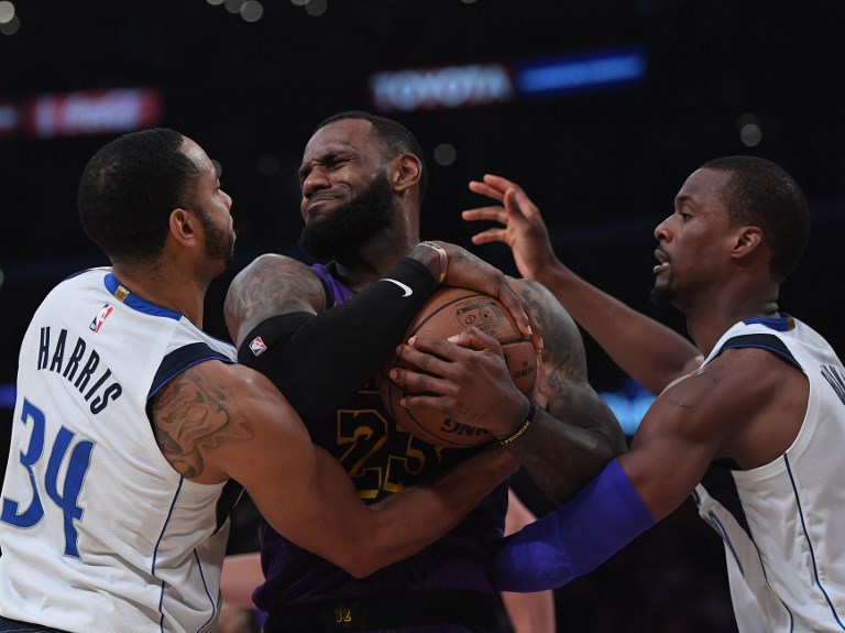 LeBron James #23 of the Los Angeles Lakers hangs on to a rebound between Harrison Barnes #40 and Devin Harris #34 of the Dallas Mavericks during a 114-103 Laker win at Staples Center on November 30, 2018 in Los Angeles, California. PHOTO/AFP