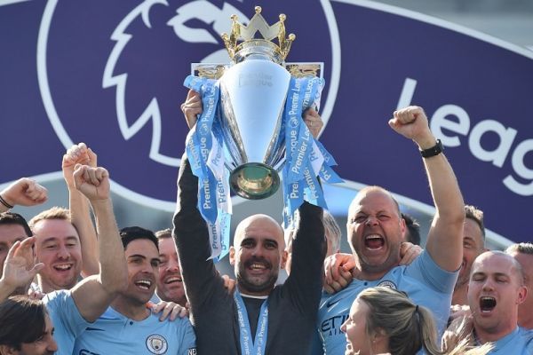 Manchester City's Spanish manager Pep Guardiola holds up the Premier League trophy as he's surrounded by his staff after their 4-1 victory in the English Premier League football match between Brighton and Hove Albion and Manchester City at the American Express Community Stadium in Brighton, southern England on May 12, 2019. PHOTO/AFP