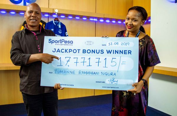 Mshindi wa Jackpot Bonus, Jumanne Ramadhani (kushoto) akikabidhiwa mfano wa hundi ya Tsh 17,771,715/= na meneja mahusiano wa SportPesa, Bi Sabrina Msuya katika ofisi za SportPesa jijini Dar es Salaam. (Picha na SP News)