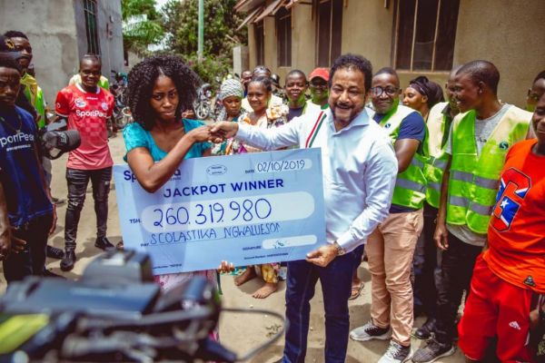 Scolastika Ngwaluesoni akikabidhiwa mfano wa hundi ya Tsh 260,319,980 na Mkurugenzi wa Utawala na Udhibiti wa SportPesa, Ndugu Tarimba Abbas nyumbani kwake, Mbagala Chamanzi jijini Dar es Salaam. (Picha na SportPesa News)