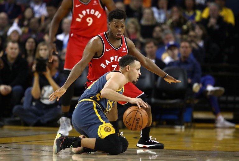 Stephen Curry of the Golden State Warriors dribbles on his knees while being guarded by Kyle Lowry of the Toronto Raptors at ORACLE Arena on December 12, 2018 in Oakland, California. PHOTO/AFP